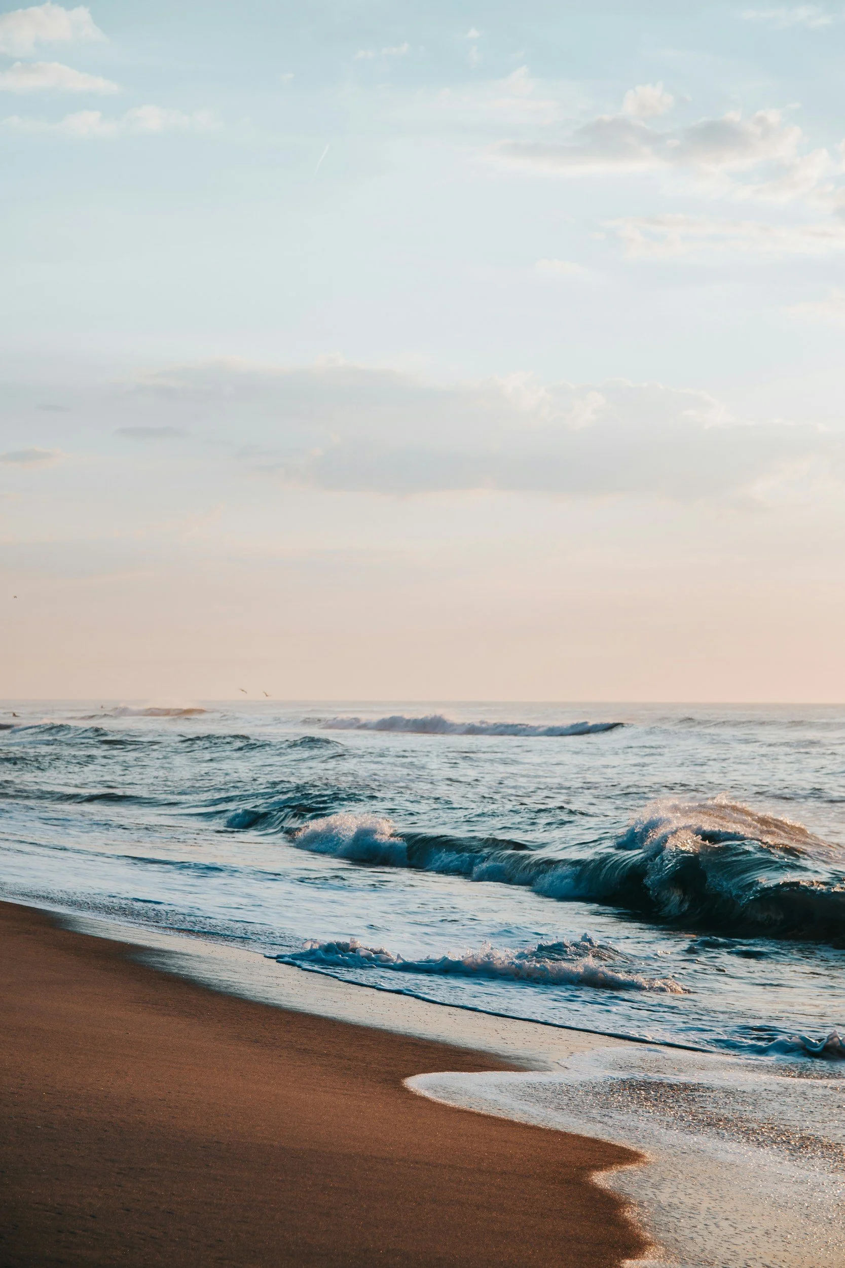 Sunset over the ocean with gentle waves and a sandy beach in the foreground.