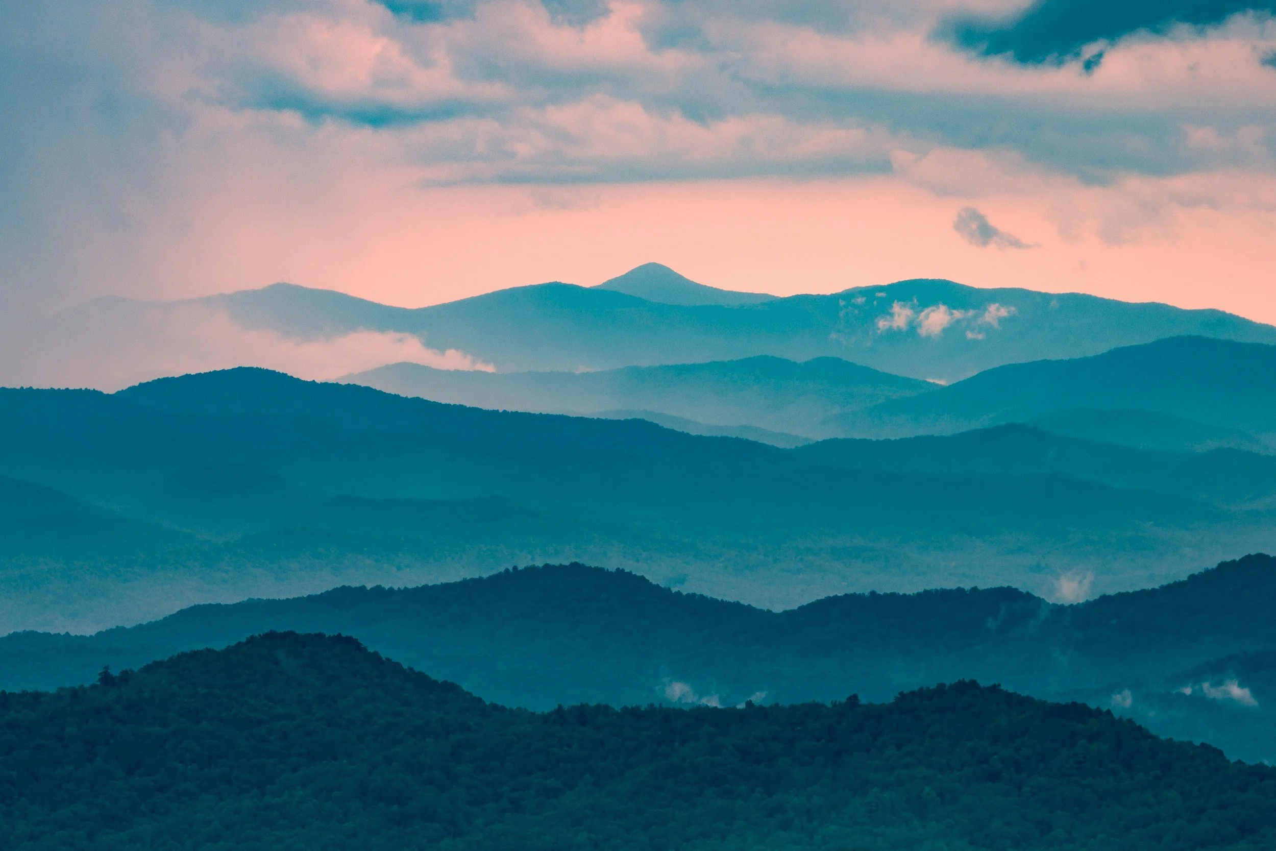 Layered mountain range with mist and clouds during sunset or sunrise, pink and blue sky.