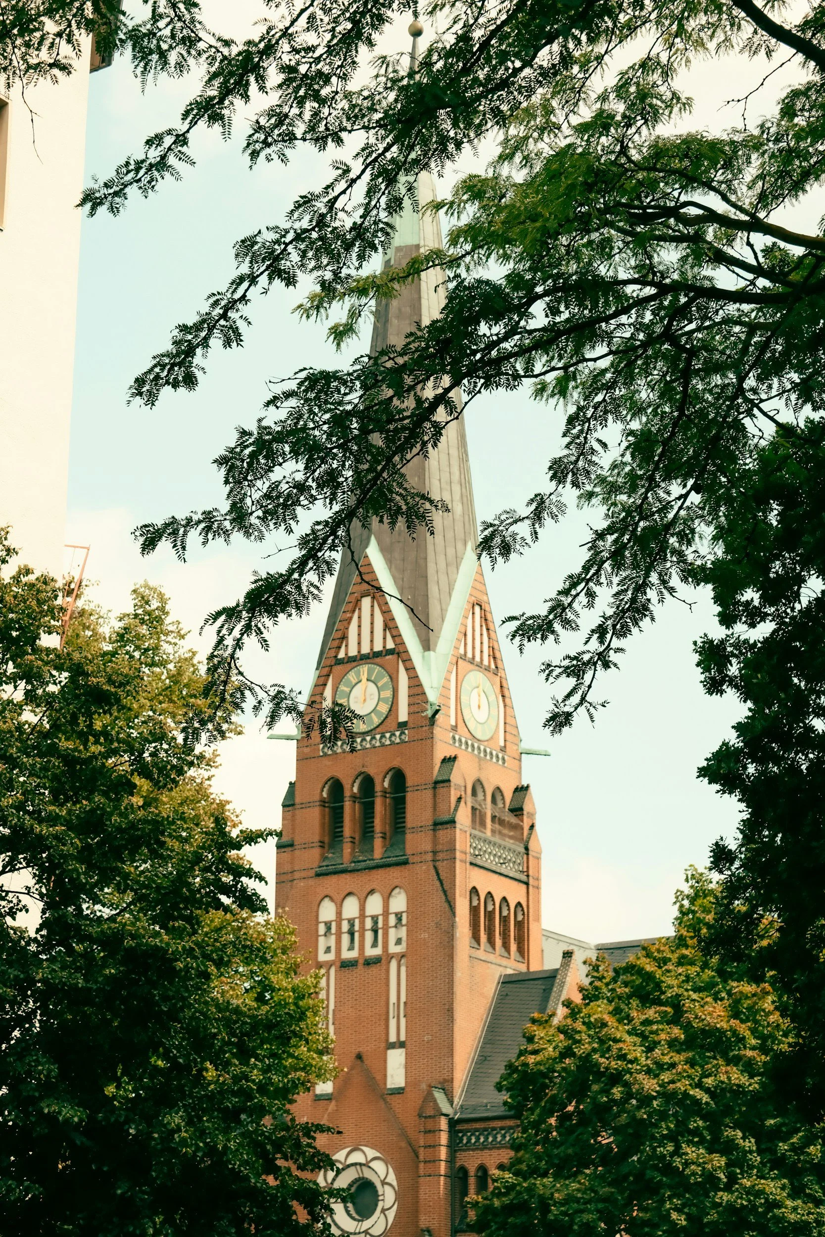 A historic brick church with a tall clock tower surrounded by green trees.