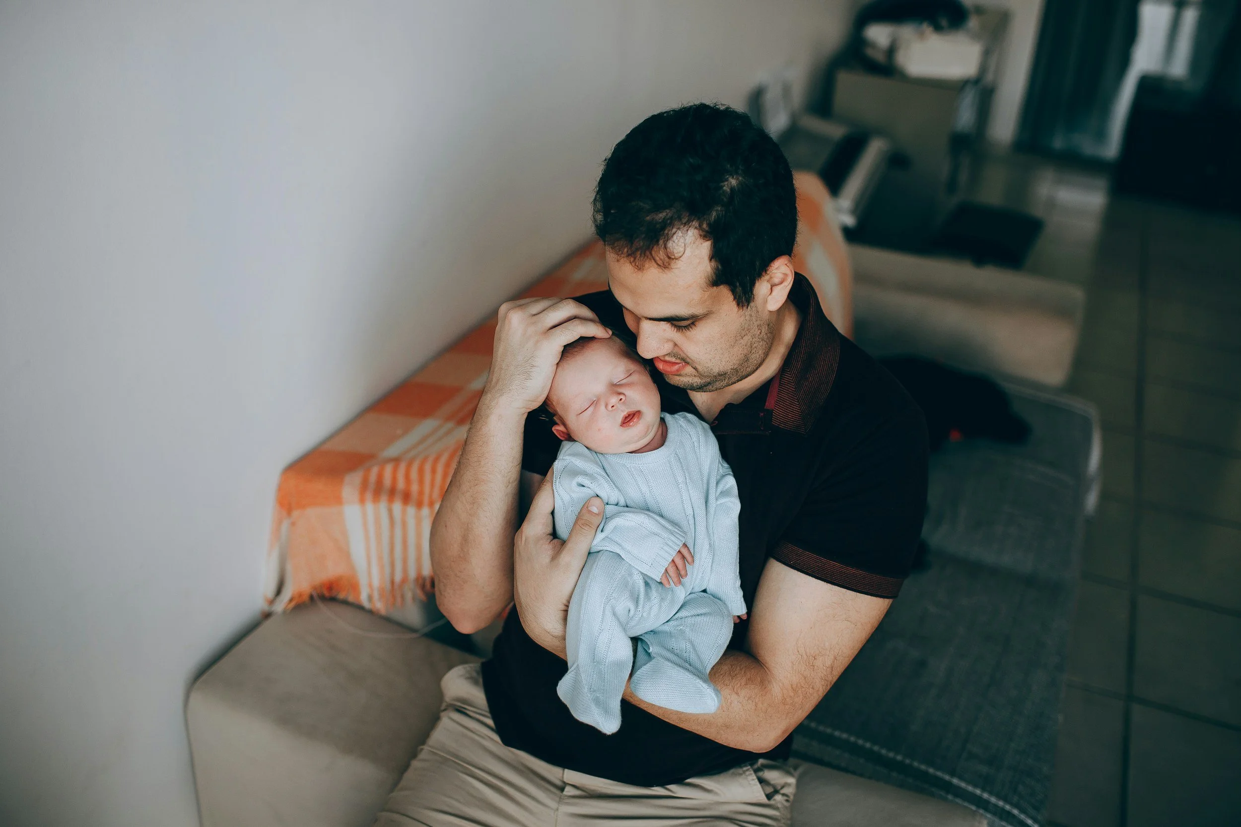 Man holding a sleeping baby while sitting on a bench in a public space.