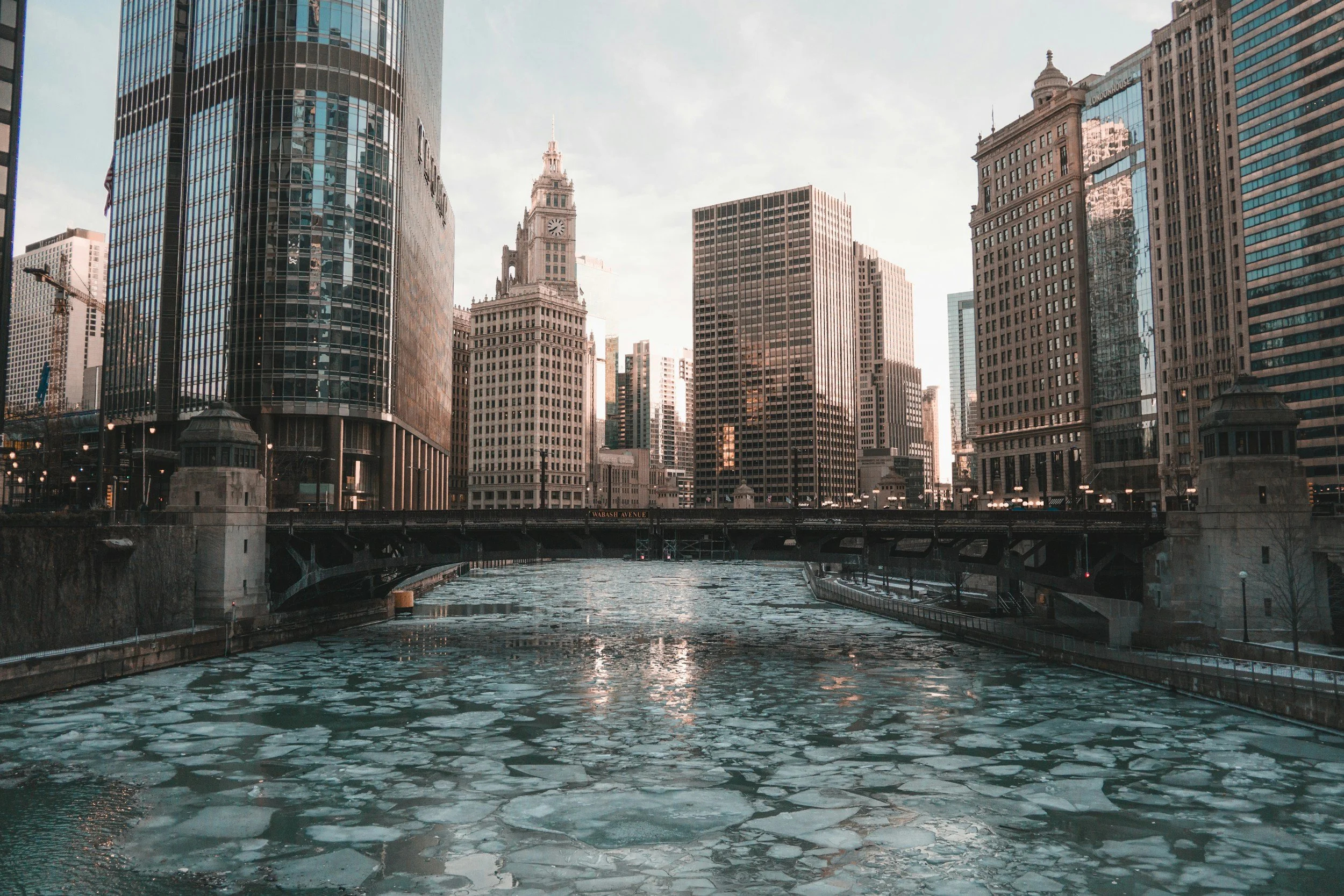 Cityscape of Chicago skyline with tall skyscrapers and a river in the foreground, partially frozen with ice floes.
