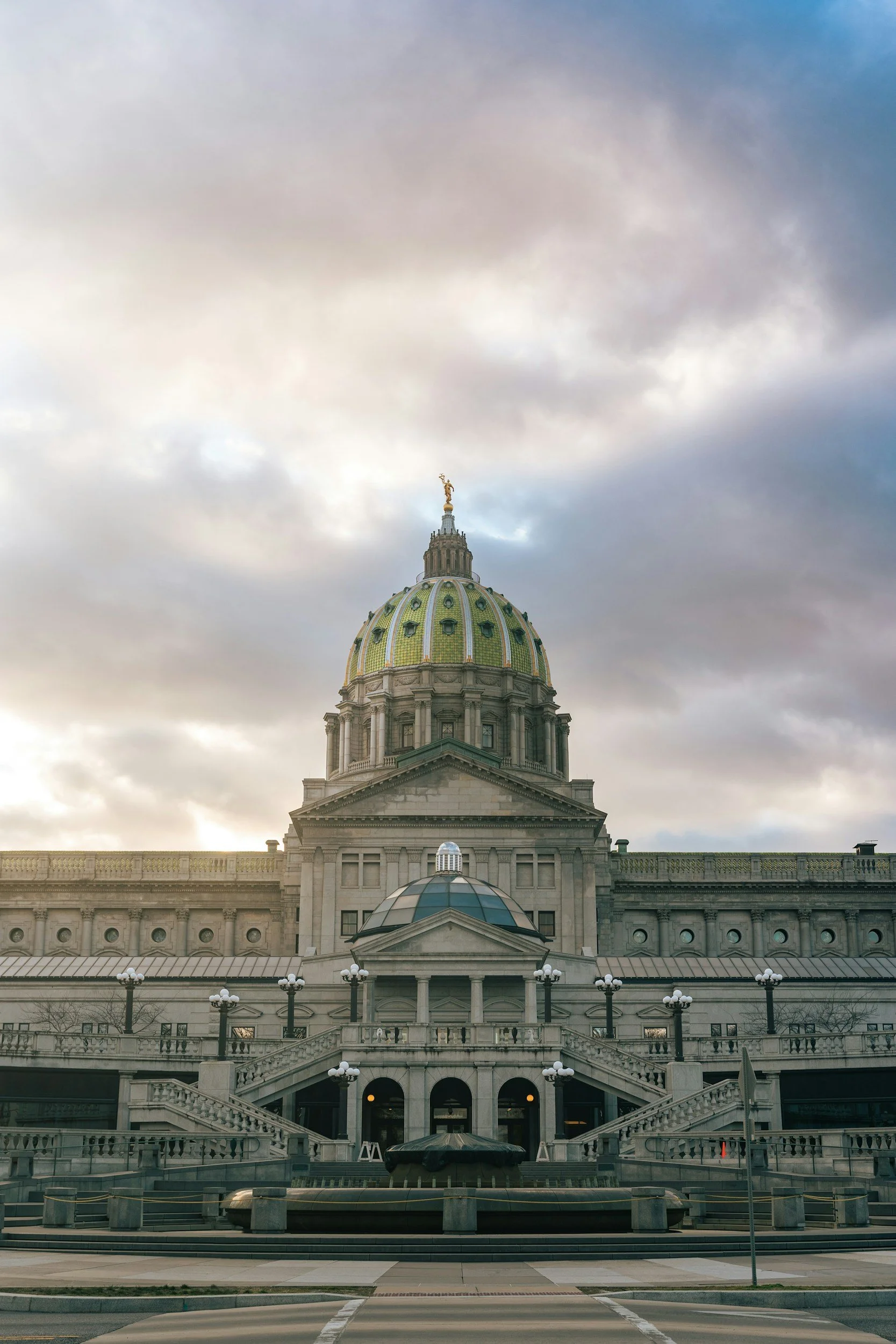 The image shows the front facade of a historic building with a large dome topped by a golden statue, set against a cloudy sky.