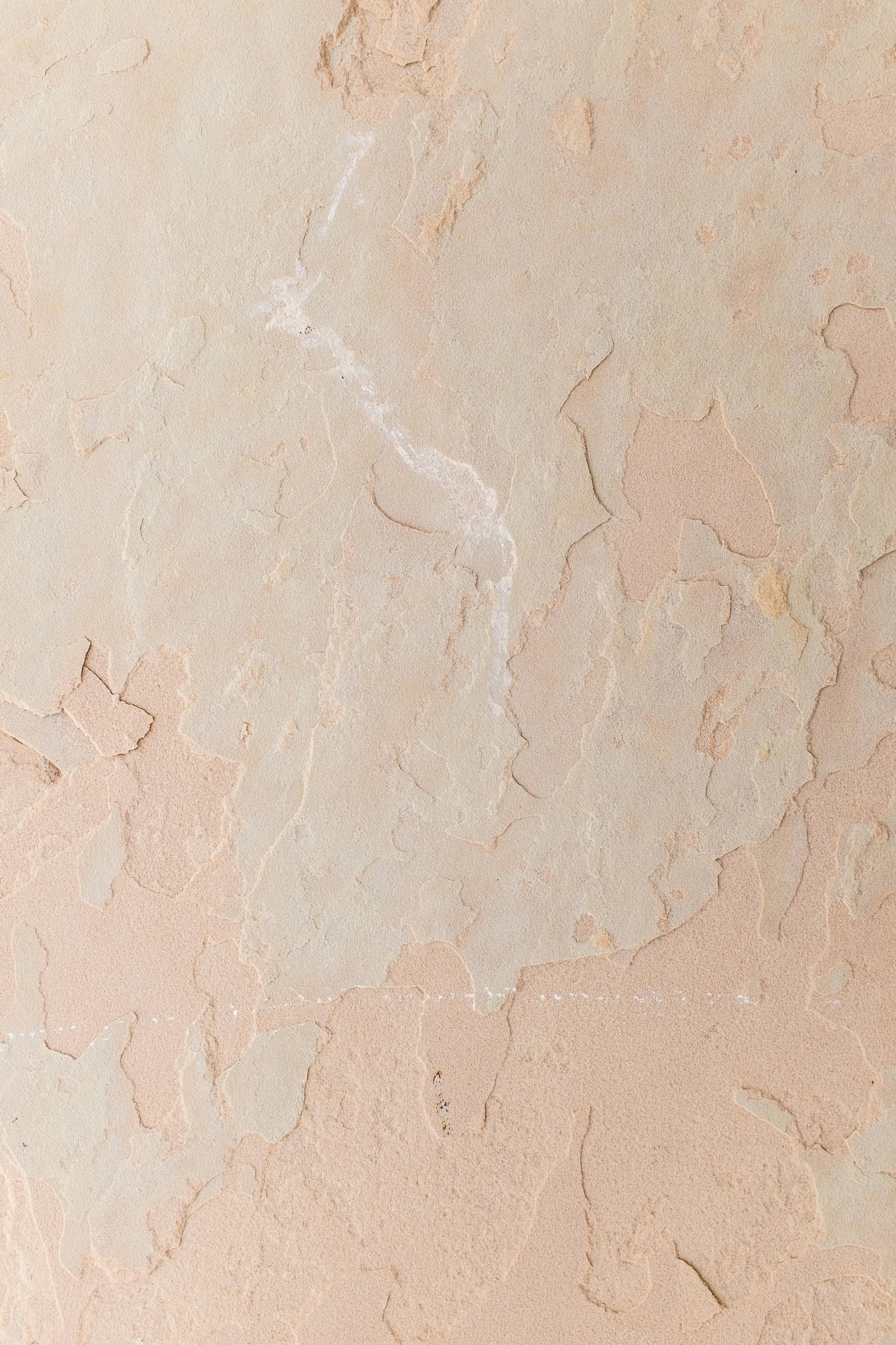 Close-up view of a textured beige plaster wall with cracks and rough patches; suitable for a background or texture.