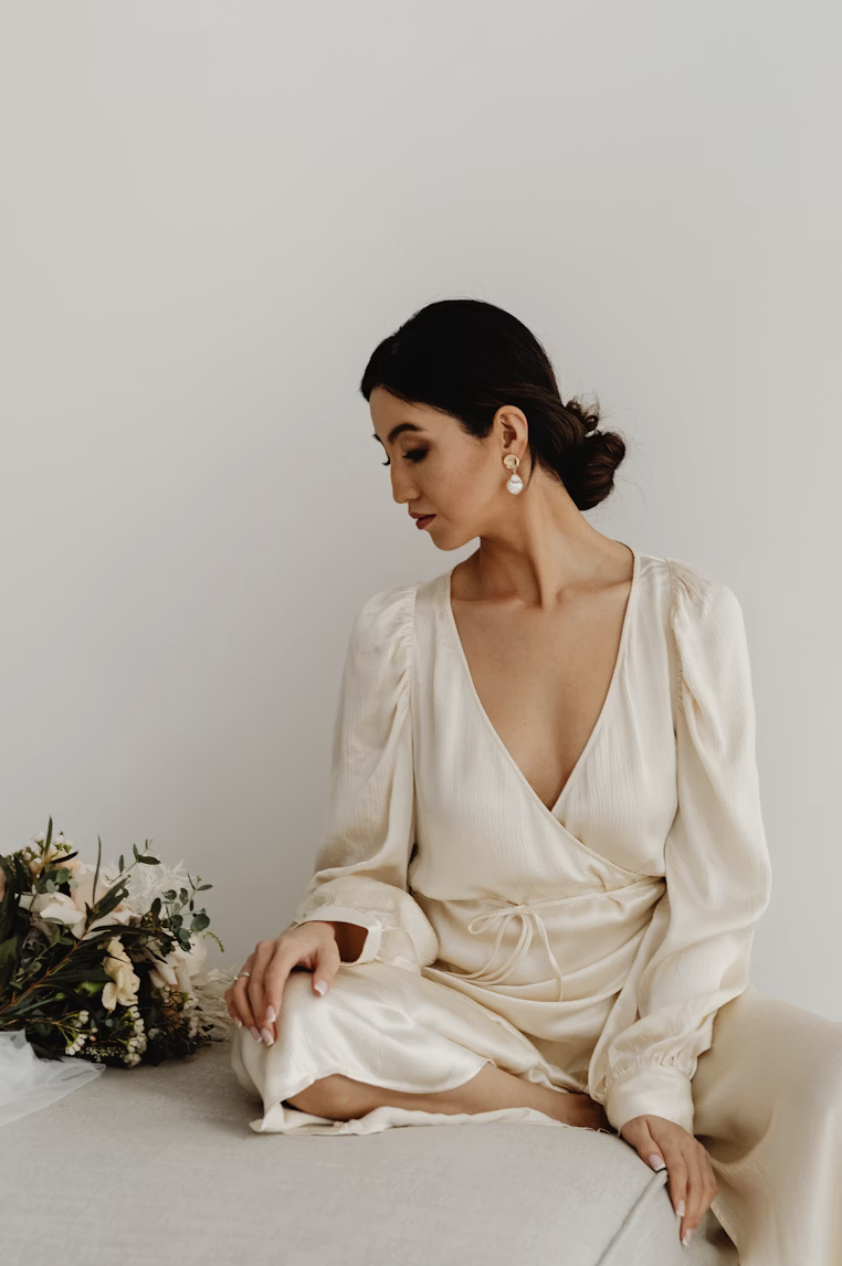 Side profile of a woman in a gray dress holding a bouquet of wildflowers and grasses against a plain background.