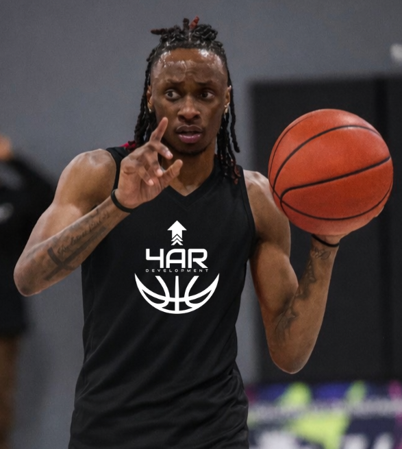 A young basketball player in a red uniform dribbling on a basketball court, with a hoop and backboard visible in the background.