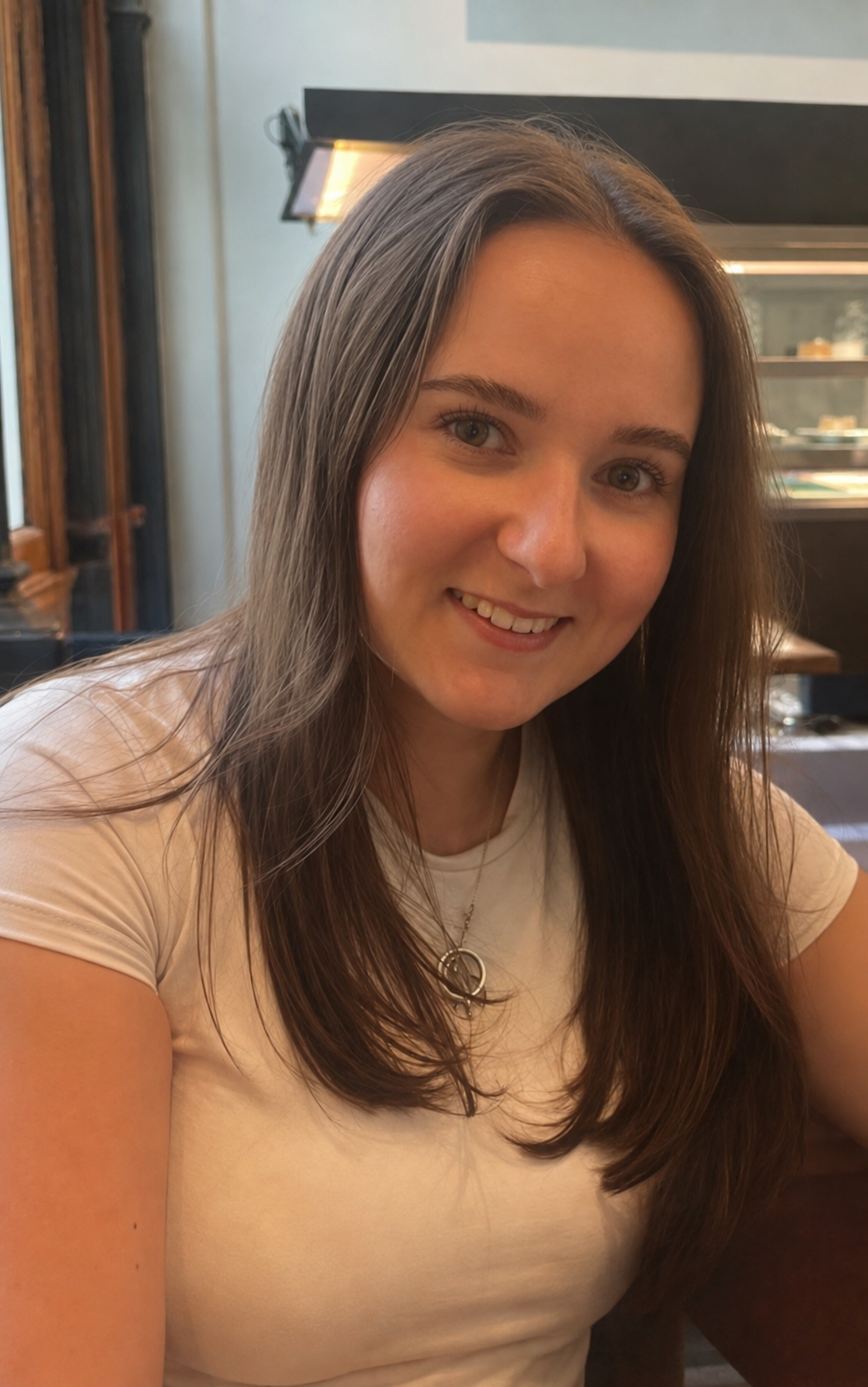 Smiling person with long hair wearing a necklace and a blue shirt.