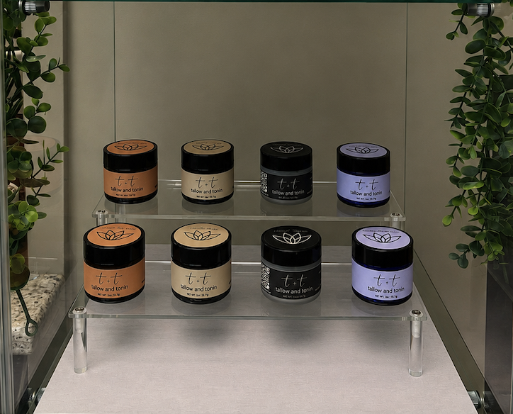 Two shelves displaying eight jars of skincare products with black lids and pastel-colored labels, surrounded by green plants.