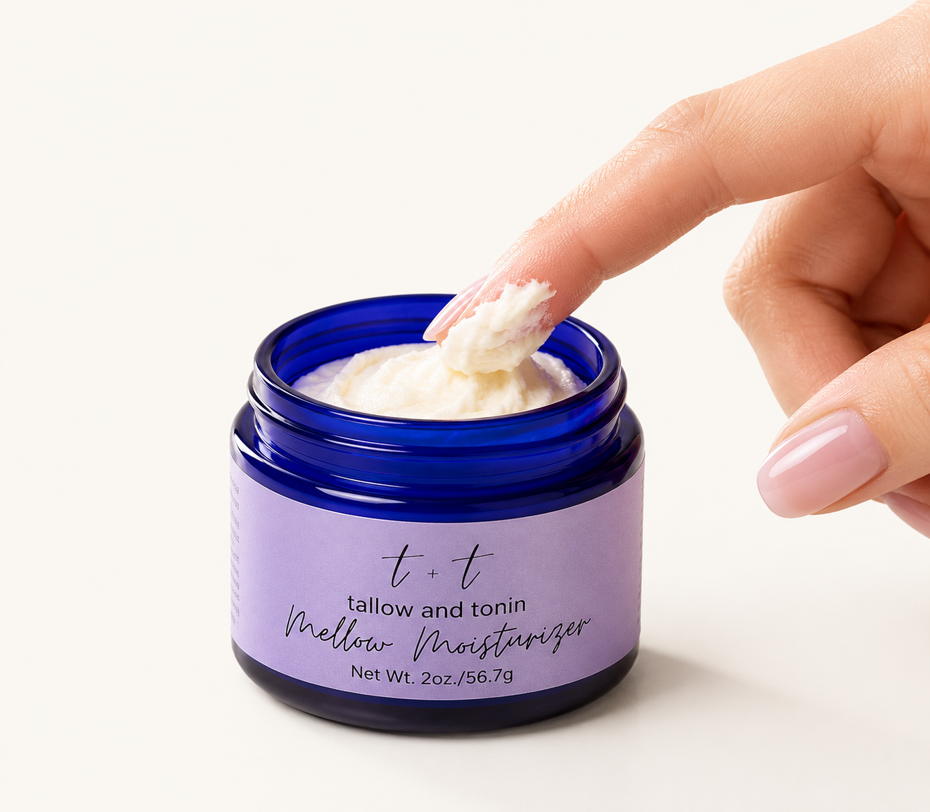 A hand dipping a finger into a blue jar labeled 't+t tallow and tonin mellow moisturizer' with cream inside.