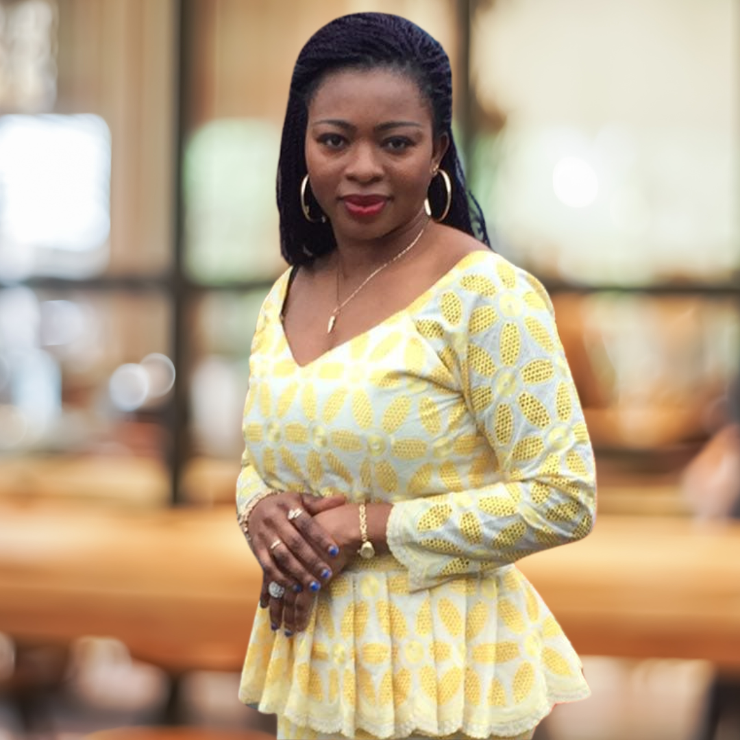 Woman wearing yellow and white floral dress with hoop earrings, standing indoors.