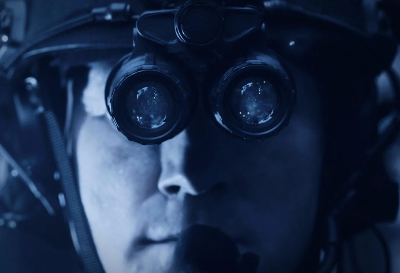 Nocturn Industries night vision shoot by CXIX: a person wearing a head-mounted device with dual binocular lenses, possibly for surveillance or scientific observation, with an intense focus expression.