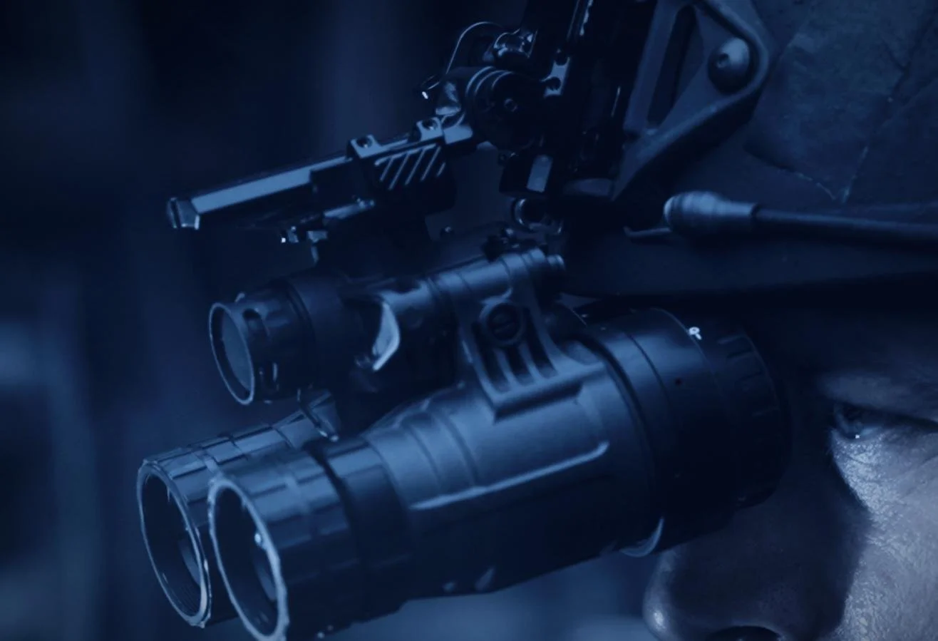 Nocturn Industries night vision shoot by CXIX: close-up of a firearm with a scope mounted on it, placed on a dark surface.
