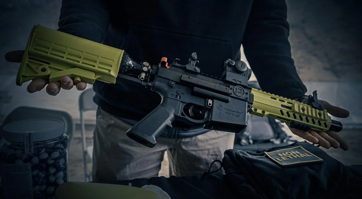 Long Island SWAT Challenge, shot by CXIX: person holding a black and olive green tactical rifle with a scope, in a room with ammunition and a bag labeled 'NON LETHAL'.