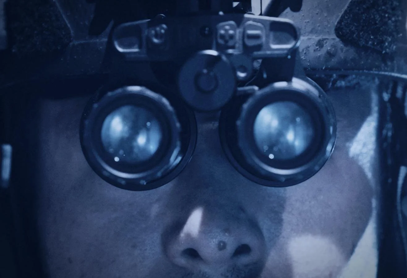 Nocturn Industries night vision shoot by CXIX: close-up of a person wearing night vision goggles, looking through binoculars or a scope.