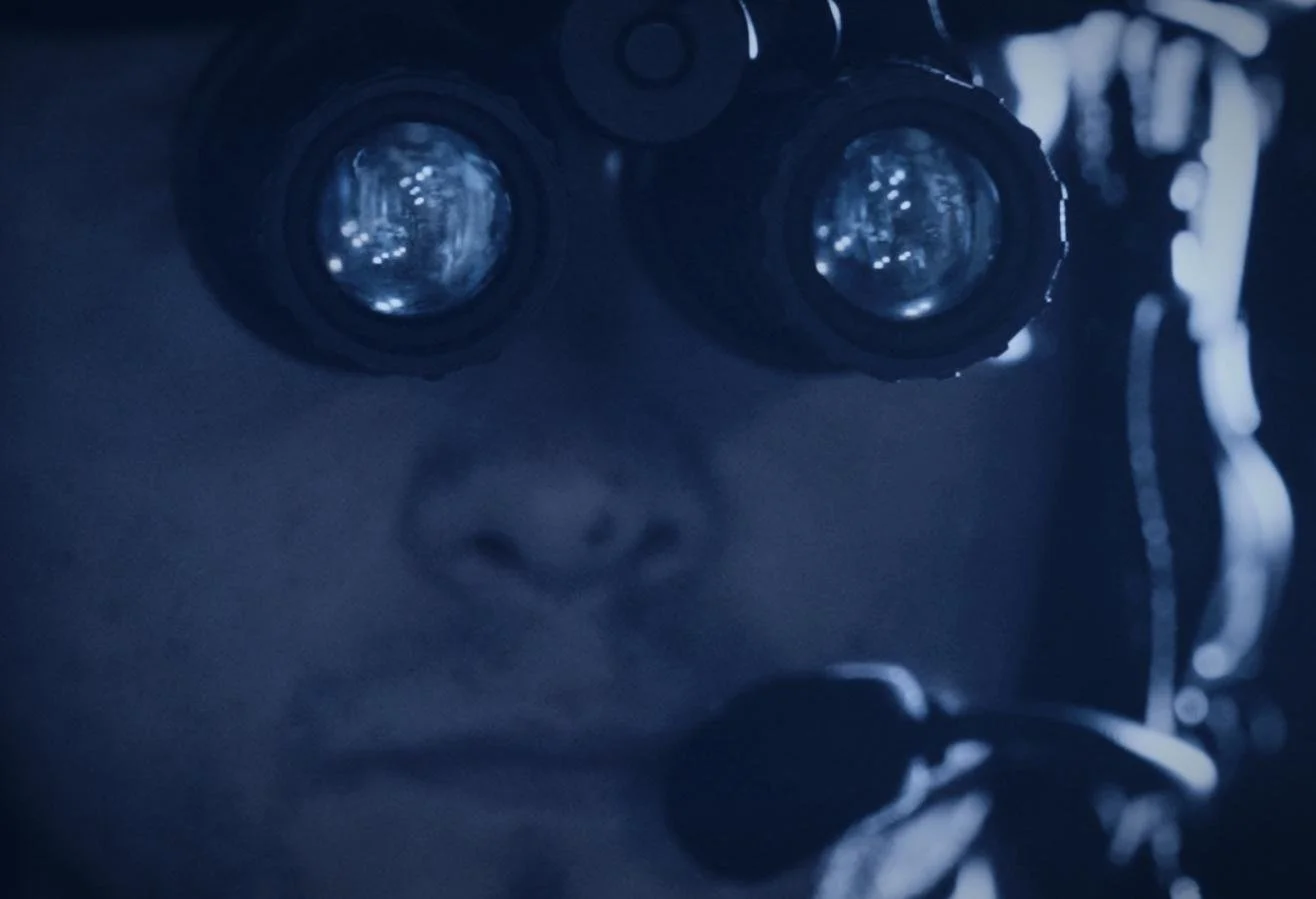 Nocturn Industries night vision shoot by CXIX: close-up of a person looking through binoculars, with only their nose and lips visible, in a dark setting.