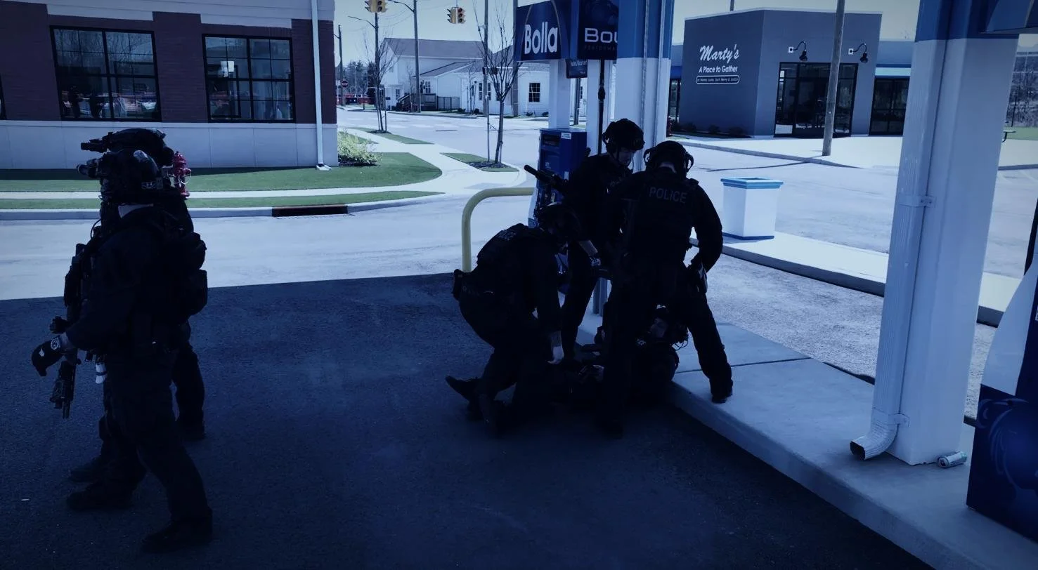 Long Island SWAT Challenge, shot by CXIX: four police officers in tactical gear inspecting or securing an area outside a building near a gas station.
