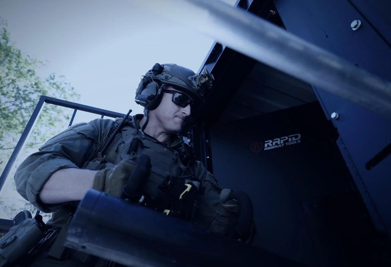 Rapid Assault Tools shoot by CXIX: a tactical soldier wearing tactical gear, sunglasses, and a helmet with a mounted camera and communication devices, operating a military or tactical vehicle.