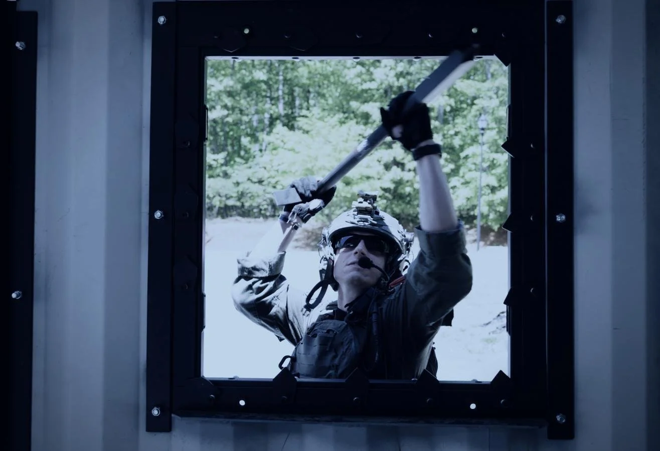 Rapid Assault Tools shoot by CXIX: a person in tactical gear and helmet using a crowbar to pry open a window from the outside, with trees visible in the background.