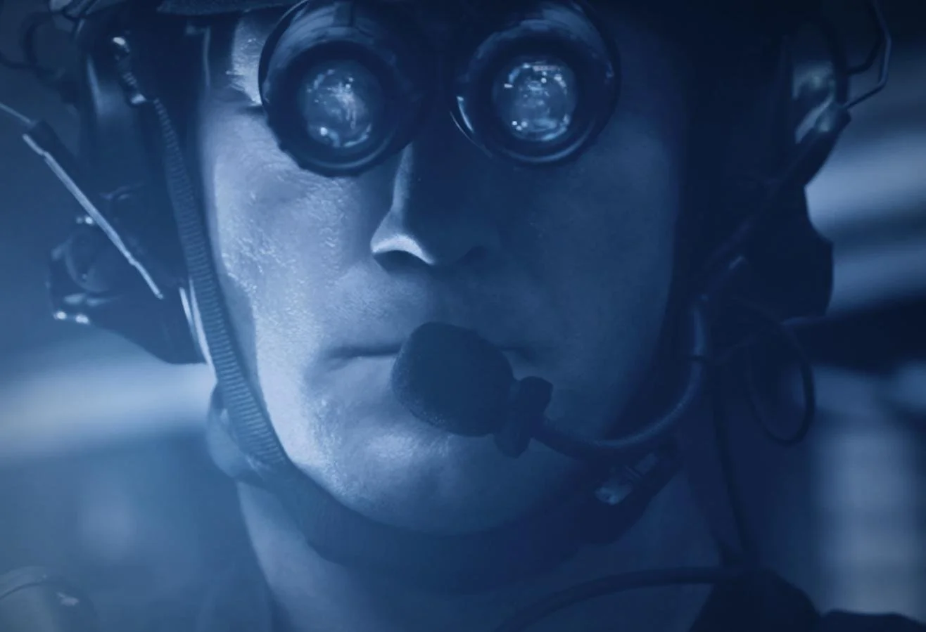 Nocturn Industries night vision shoot by CXIX: close-up of a person wearing pilot goggles and a headset, looking focused, in a blue-tinted scene.