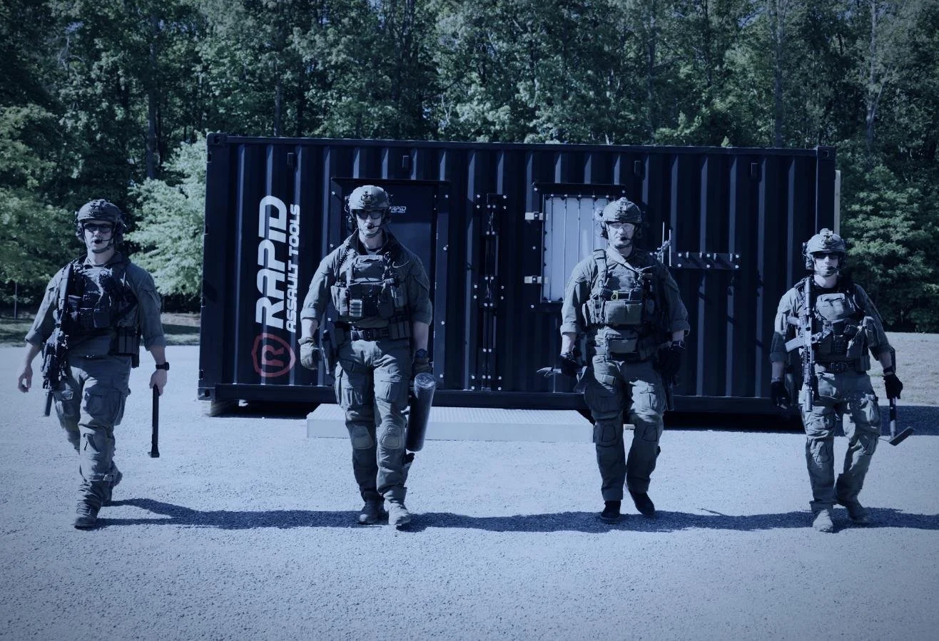 Rapid Assault Tools shoot by CXIX: four soldiers in tactical gear walking out in front of a black shipping container with trees in the background.