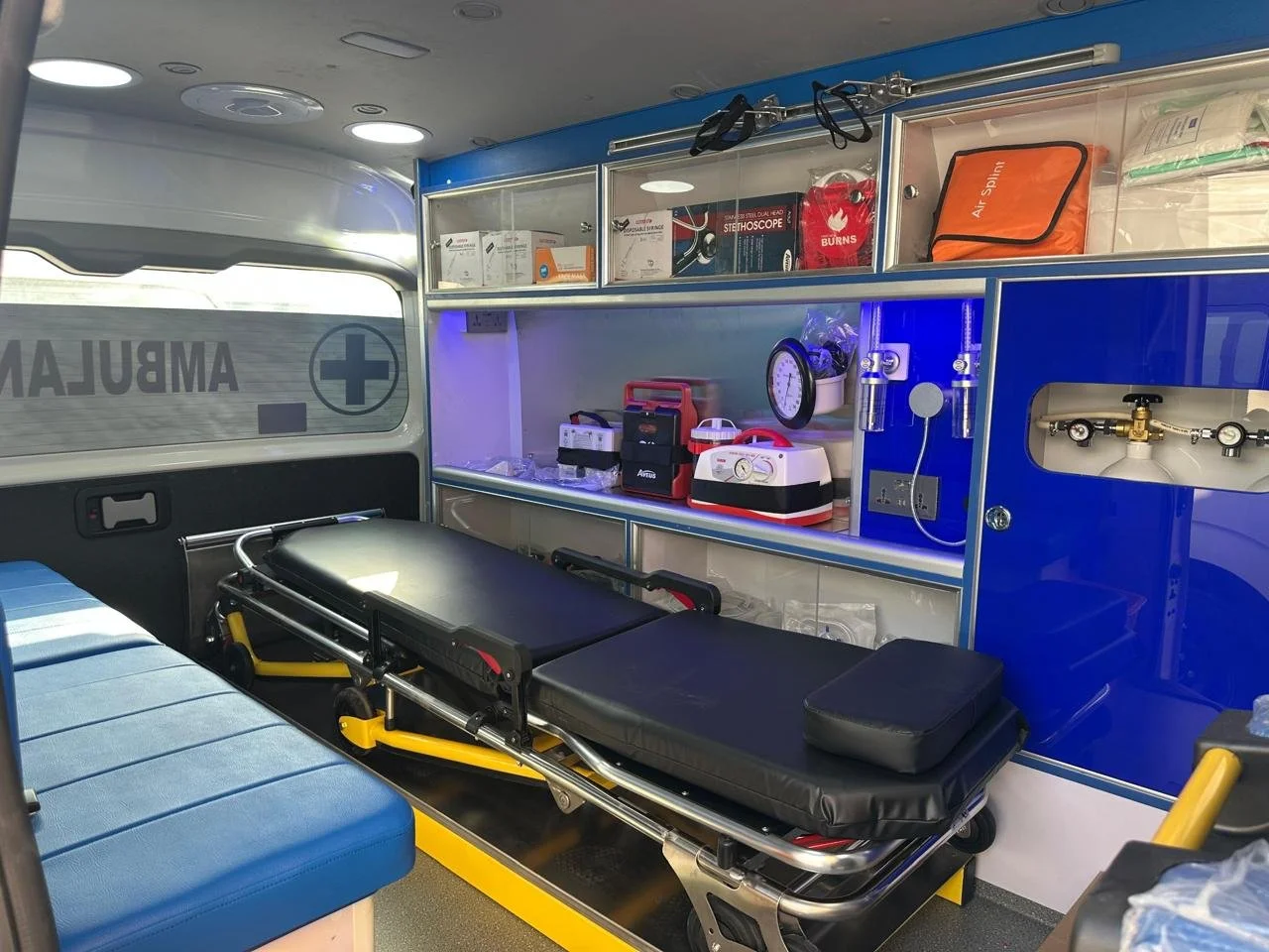 Interior of an ambulance with medical equipment, stretcher, and emergency supplies organized on shelves.