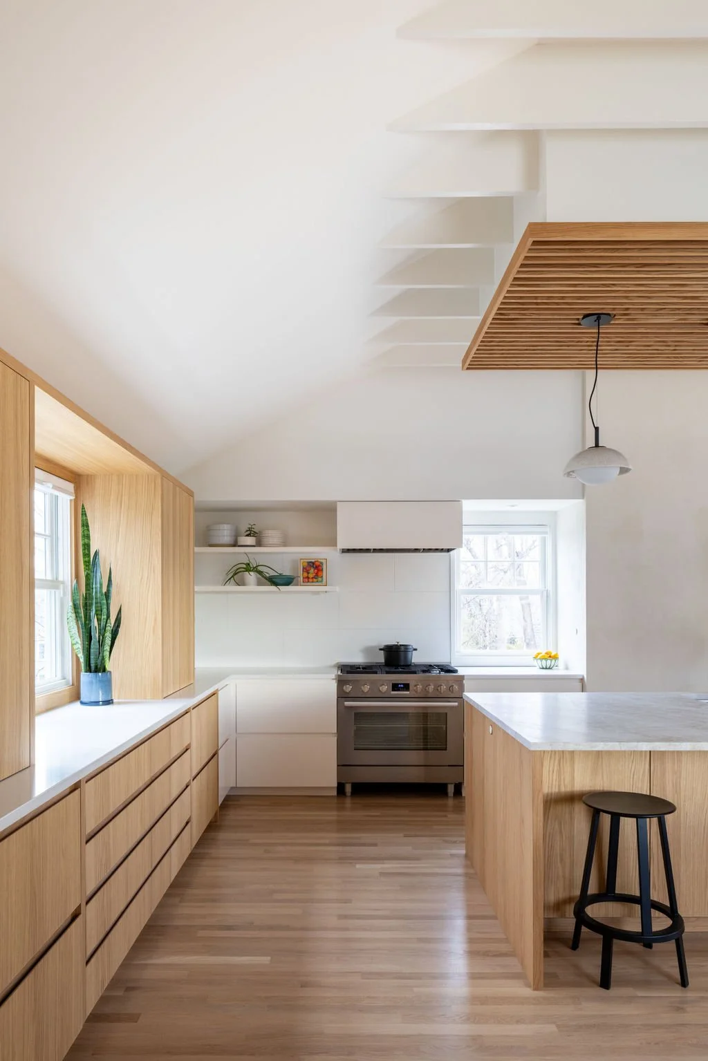 White oak kitchen cabinetry and quartzite island beneath vaulted ceiling with exposed beam details.
