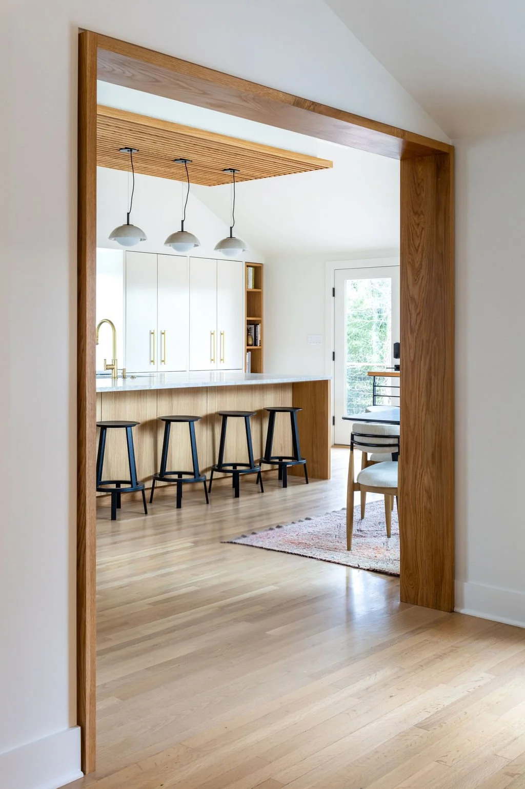 View through white oak ribbon threshold into modern kitchen with large island and slatted oak ceiling feature.