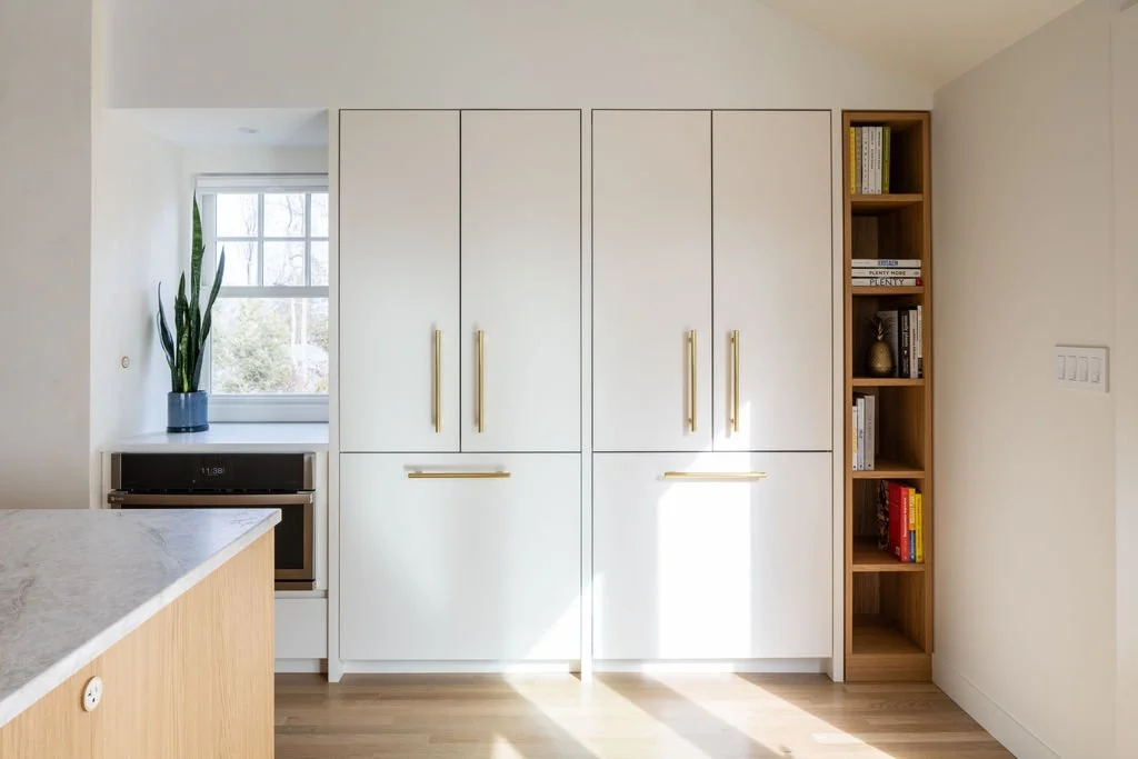 Tall white kitchen cabinetry with aged brass hardware and integrated appliances.