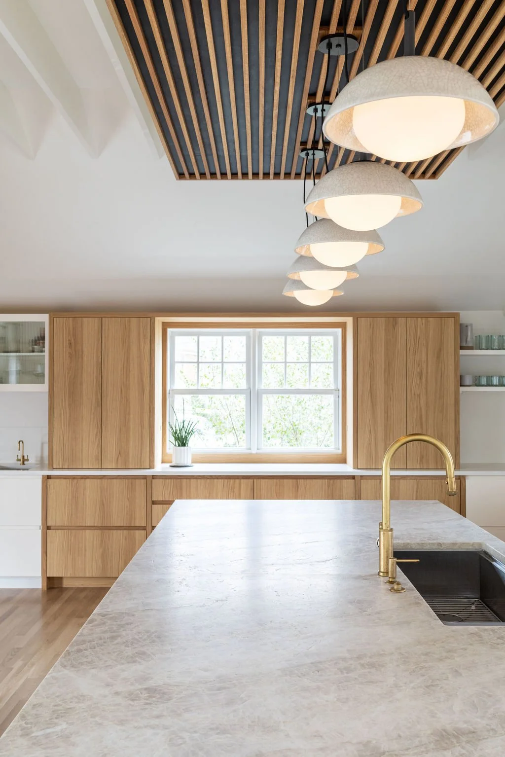 Kitchen island with Taj Mahal quartzite countertop and aged brass faucet in modern oak kitchen renovation.