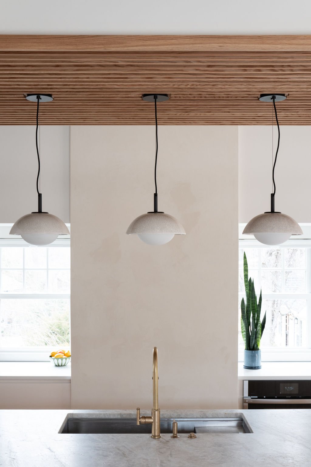 Pendant lights and slatted oak ceiling detail above quartzite kitchen island and Venetian plaster chimney.