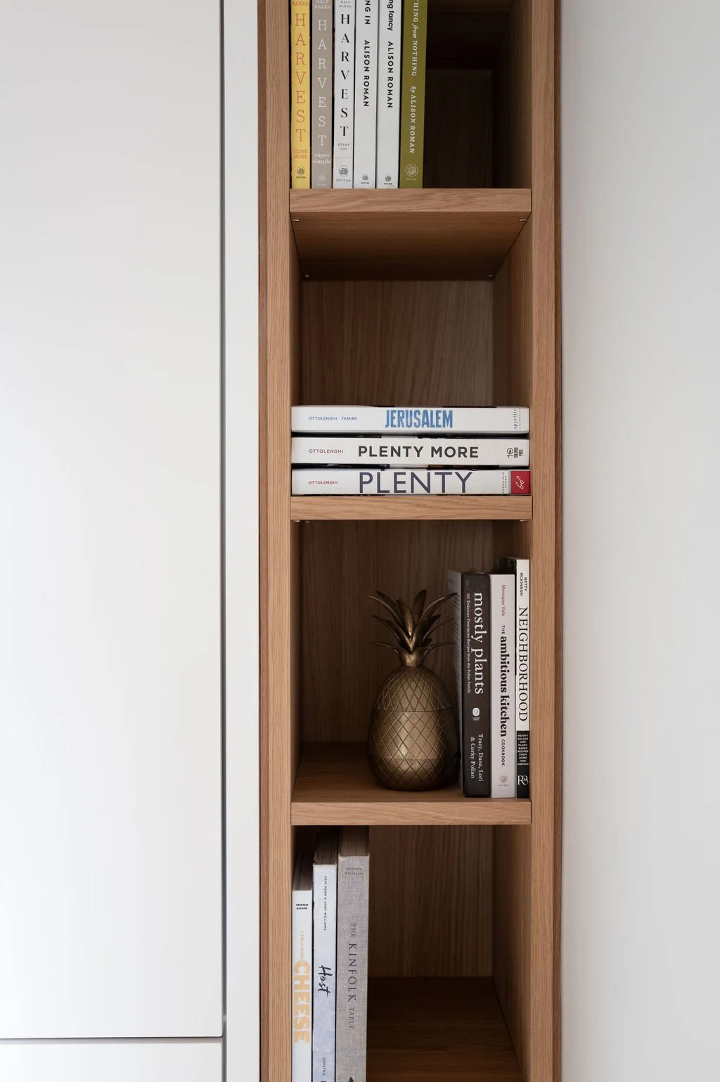 Built-in white oak shelving with cookbooks and decorative objects beside kitchen cabinetry.