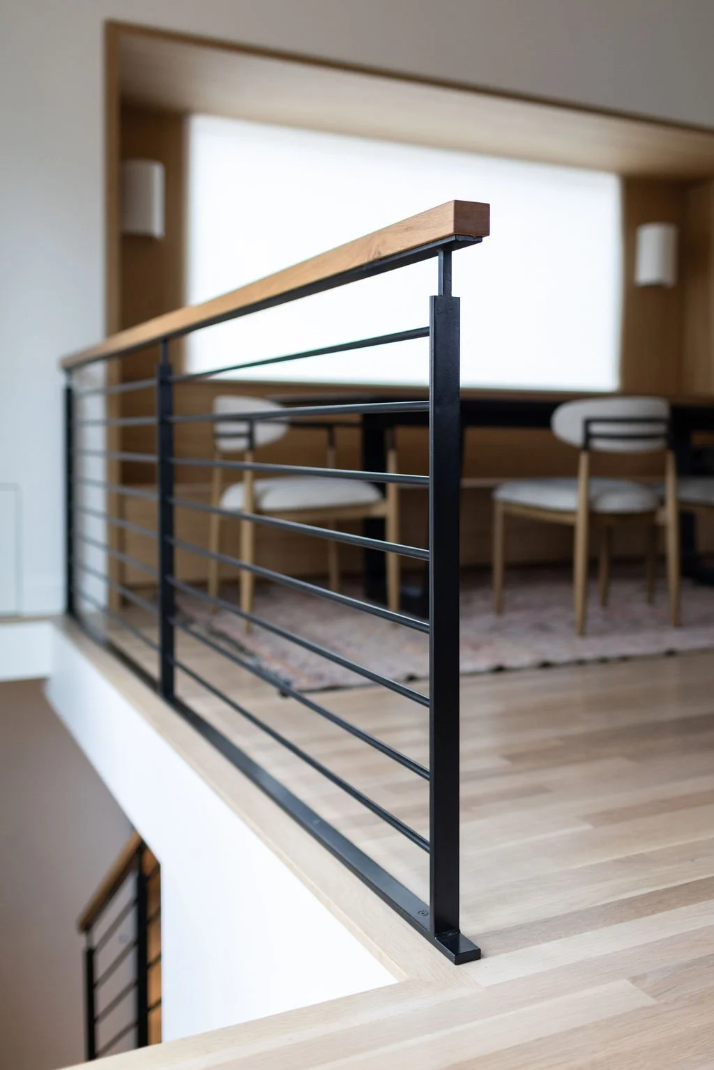 Custom steel and white oak stair railing overlooking banquette dining area.