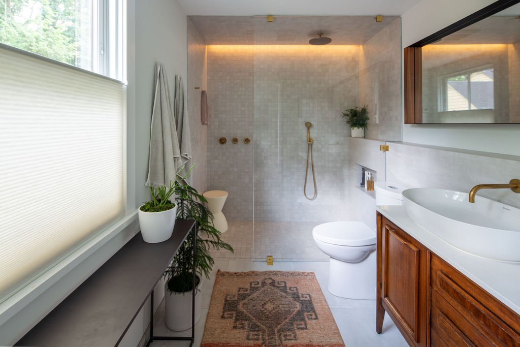 Modern primary bathroom with curbless shower, concealed trench drain, brass Watermark plumbing fixtures, and vintage walnut vanity.