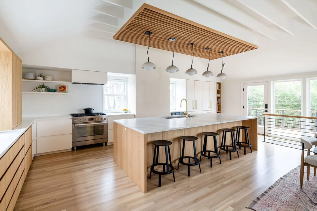 Modern family kitchen with white oak island, Taj Mahal quartzite countertop, and slatted oak ceiling feature above pendant lighting.