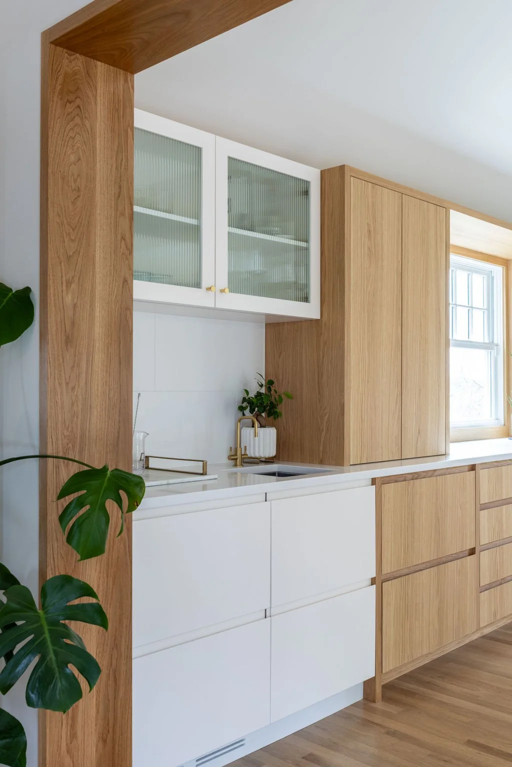 White oak and white kitchen cabinetry with integrated bar sink and fluted glass upper cabinets.