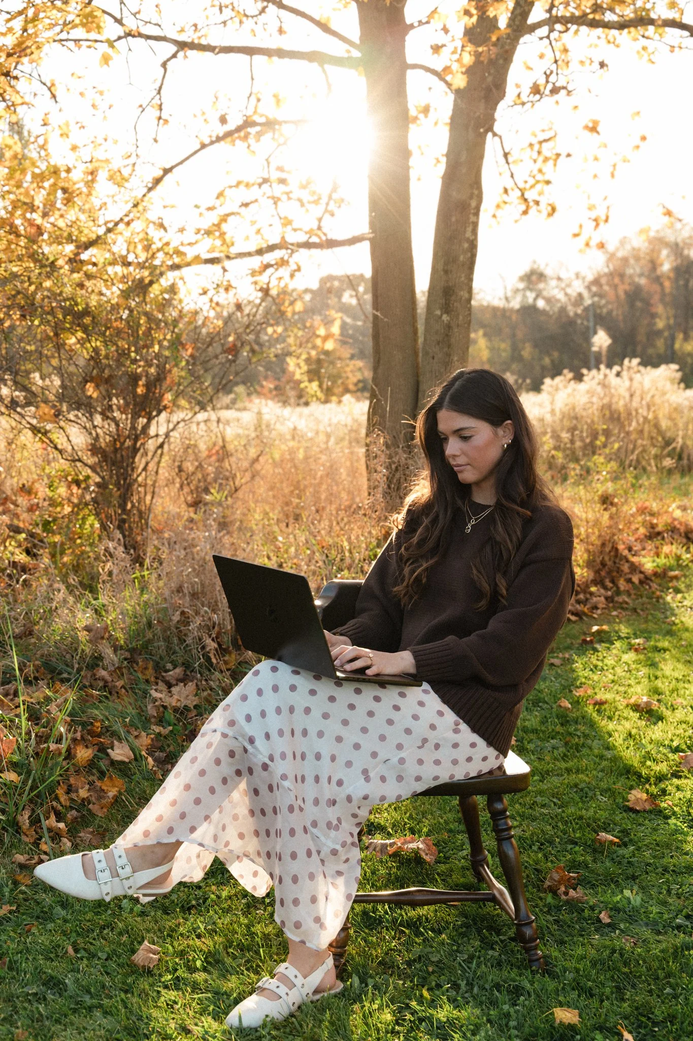 Woman using a laptop outdoors in a sunlit autumn garden