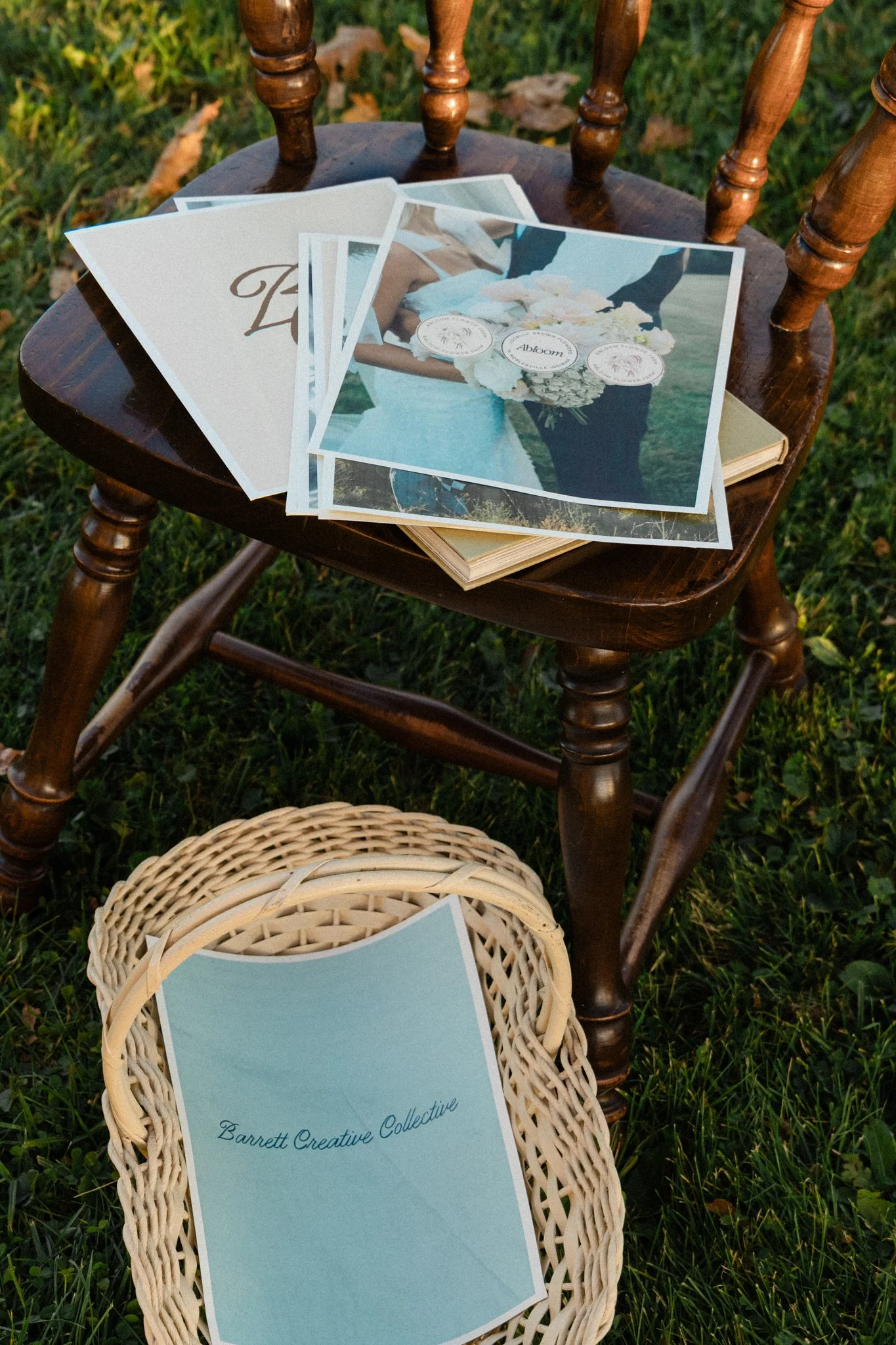 Wedding stationery and printed photos arranged on a vintage wooden chair and wicker stool outdoors on grass