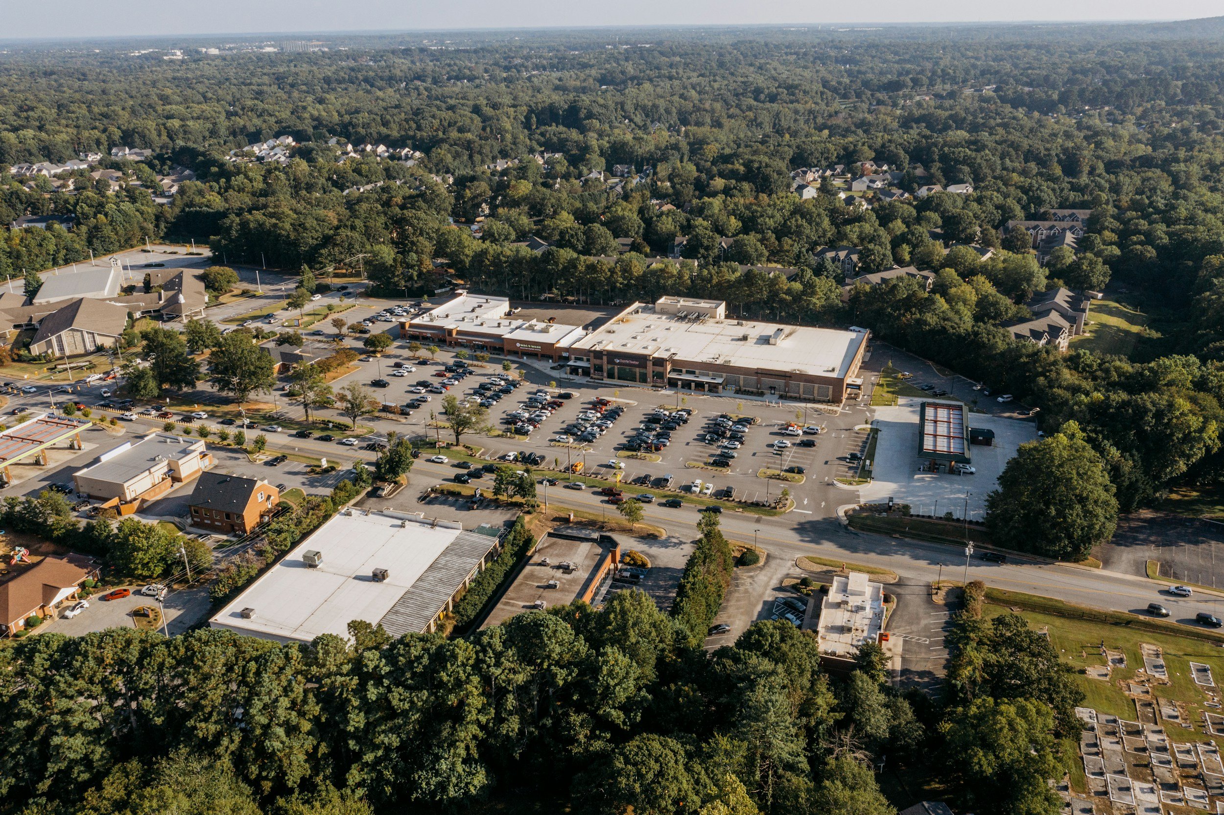 Aerial view of a grocery-anchored neighborhood shopping center with parking lot and surrounding trees