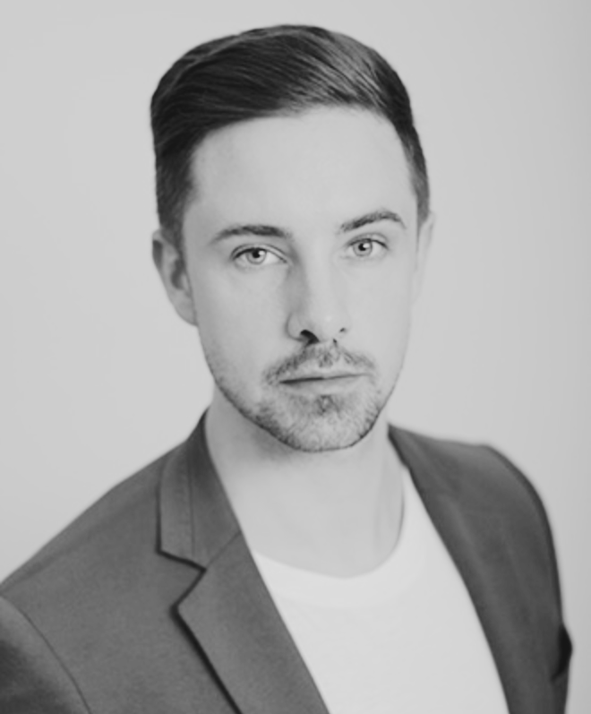 Black and white portrait of a young man with neatly styled hair, wearing a blazer and a white t-shirt, looking directly at the camera with a serious expression.