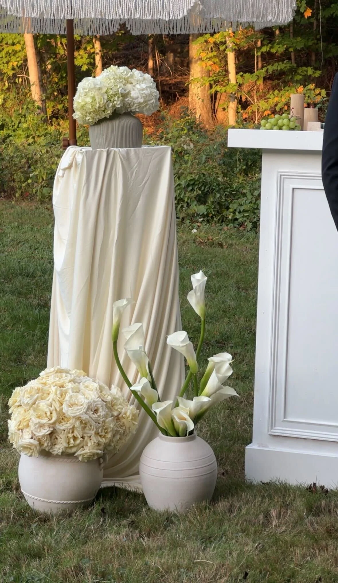 Decorative vases filled with white flowers, set outdoors with greenery in the background.