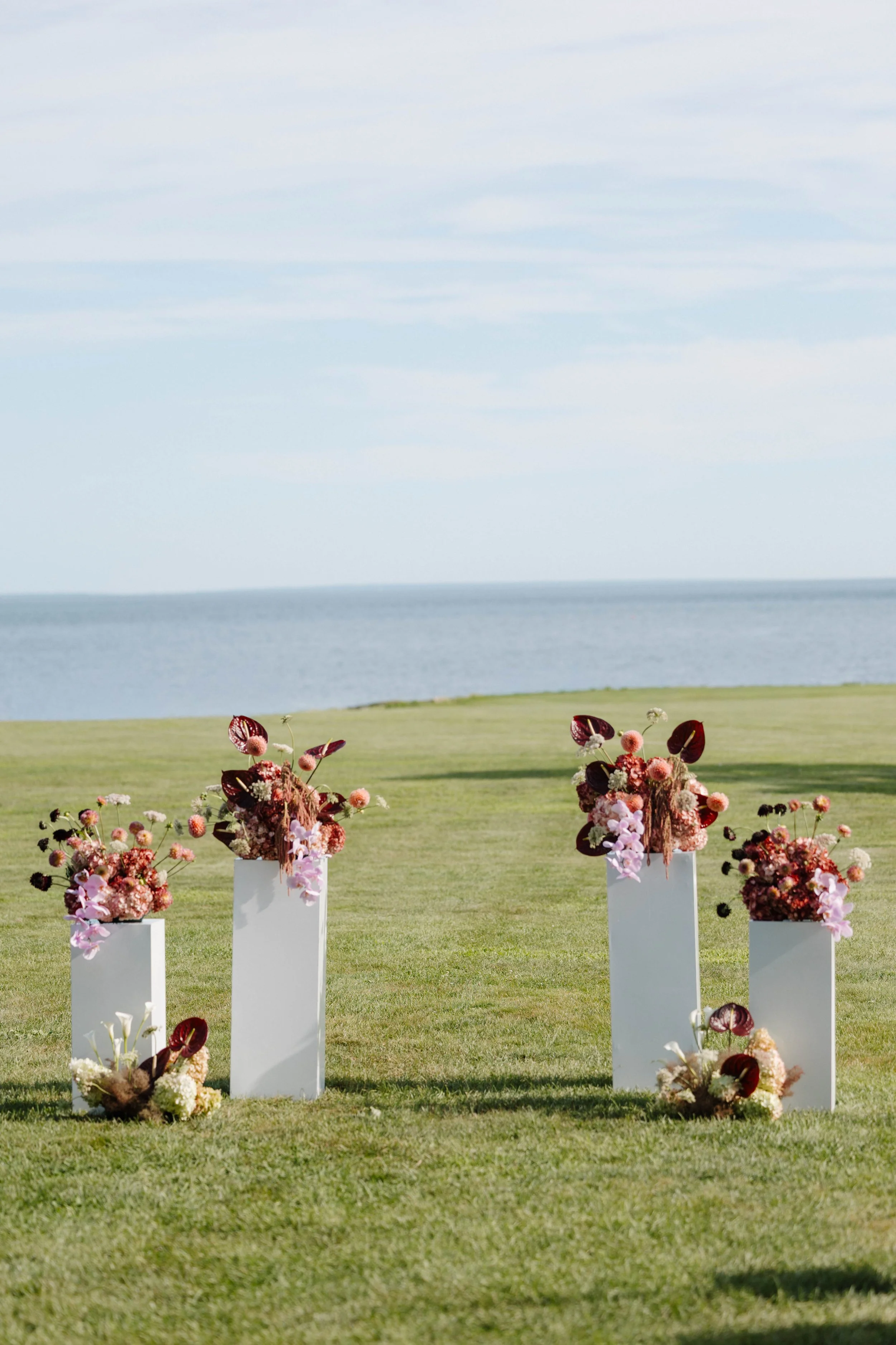 six pillar arrangements layered using tropical florals such as anthuriums and orchids. Designed with seasonal dahlias, hydrangeas, and queen annes lace in a pink and burgundy color palette. 