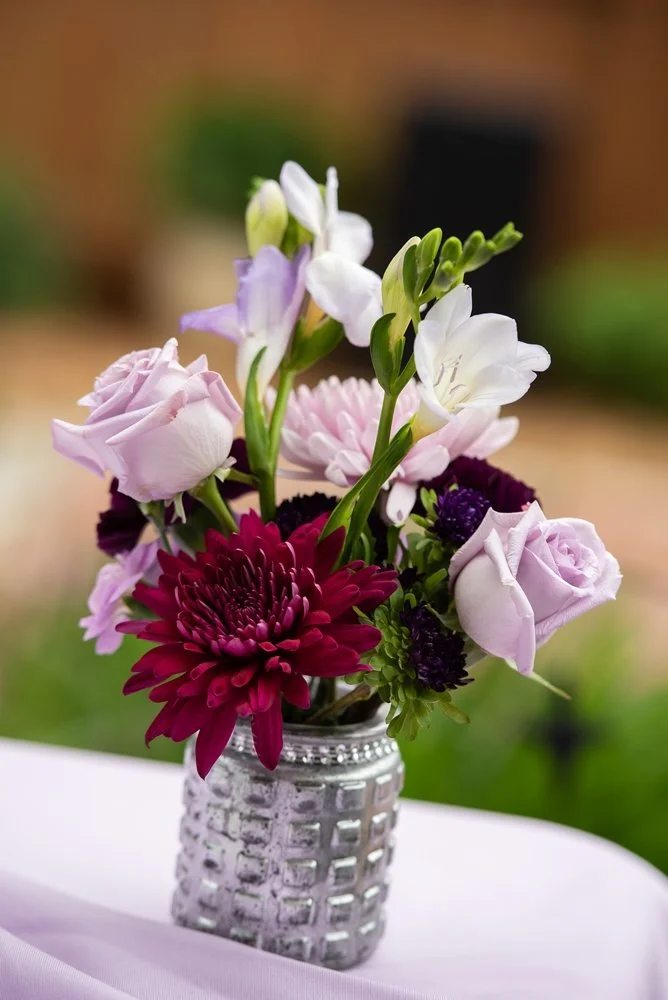 Bouquet of purple and white flowers in a silver vase on a table.