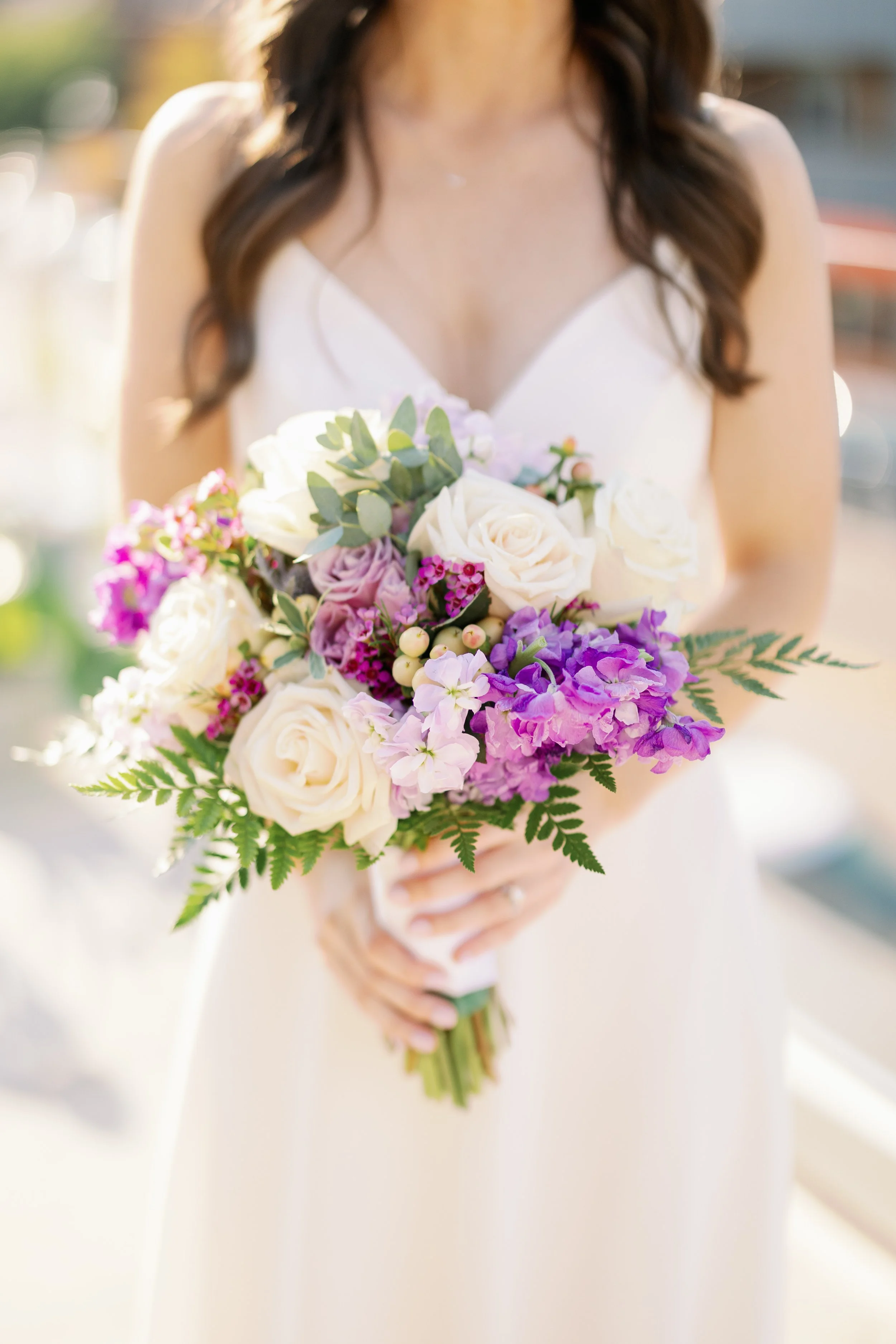 Bride holding a bouquet with white and purple flowers.