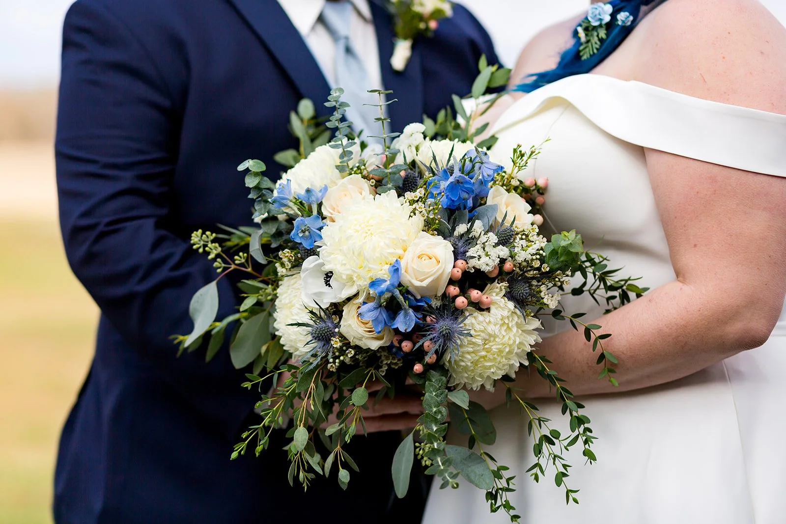 Wedding couple holding a floral bouquet with white roses and blue flowers.