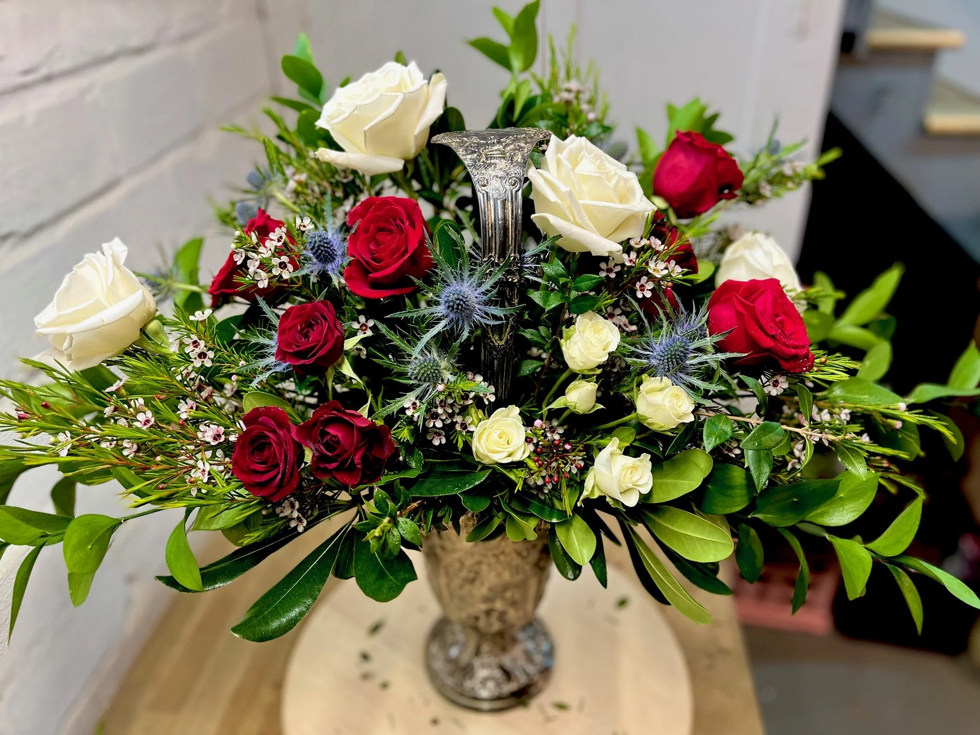 Elegant flower arrangement with red and white roses, greenery, and accent flowers in a decorative vase.