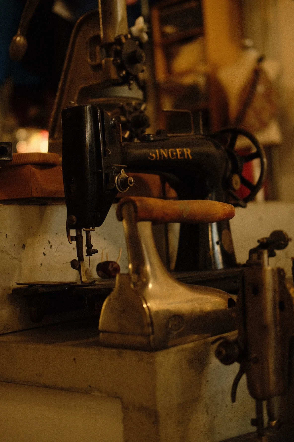 Close-up of an antique Singer sewing machine with a brass handheld iron in the foreground, set against a vintage workshop background.