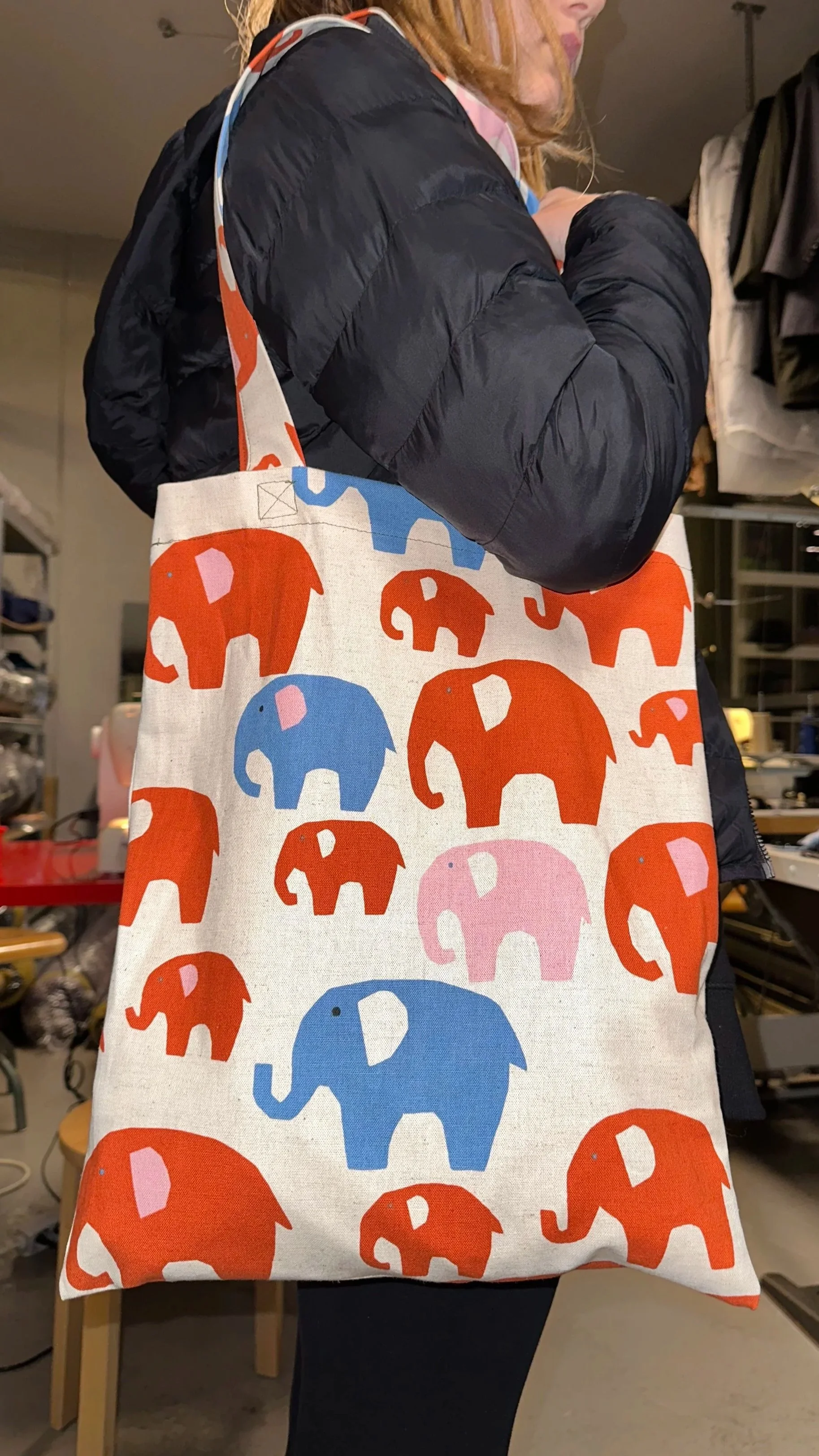 Person carrying a tote bag with a pattern of red, blue, and pink elephants.