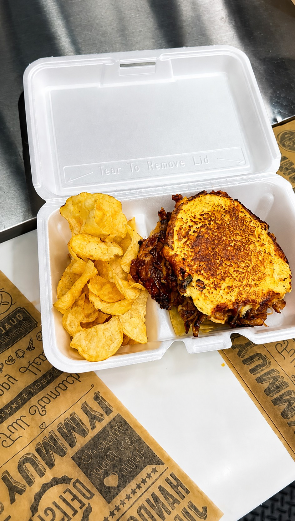 Fried potato chips and a grilled cheese sandwich in a takeout container.