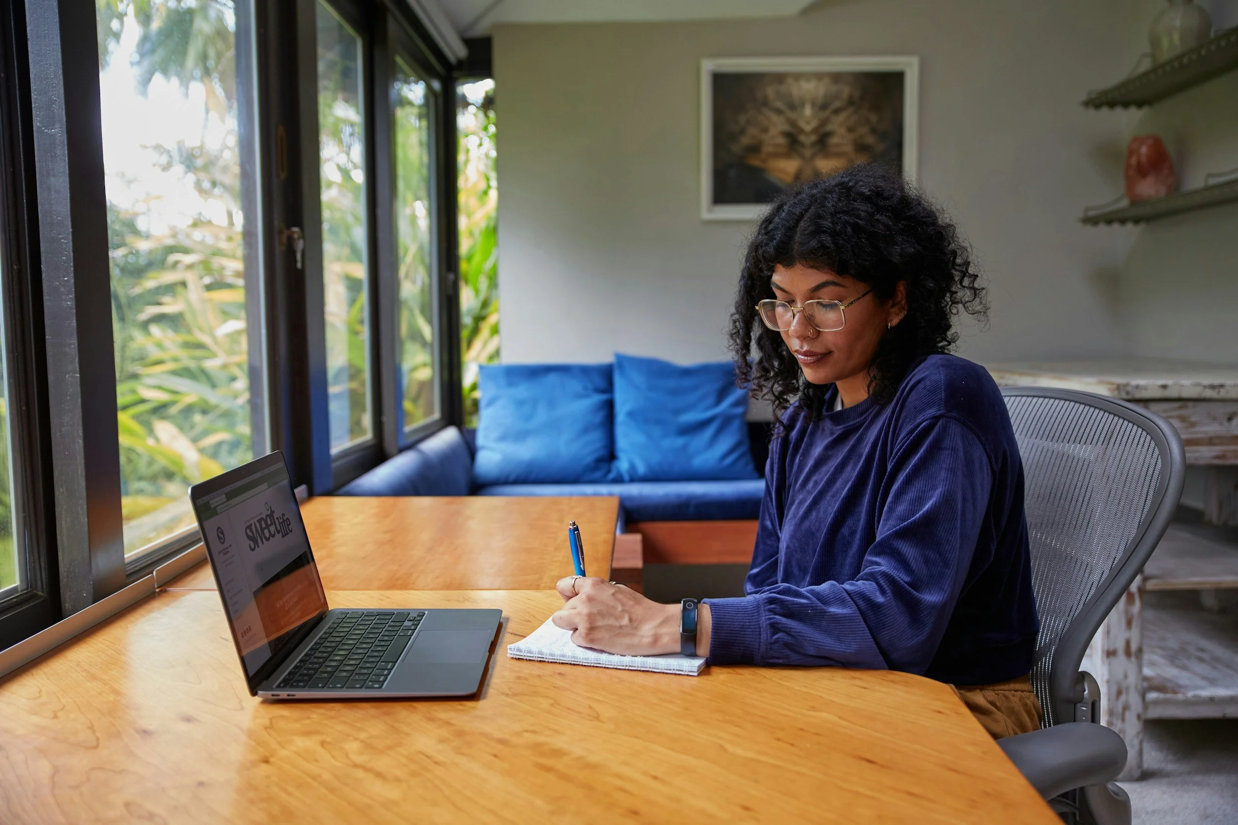 Professional woman working at a laptop and writing notes at a desk in a calm office setting, representing focused and sustainable performance at work.