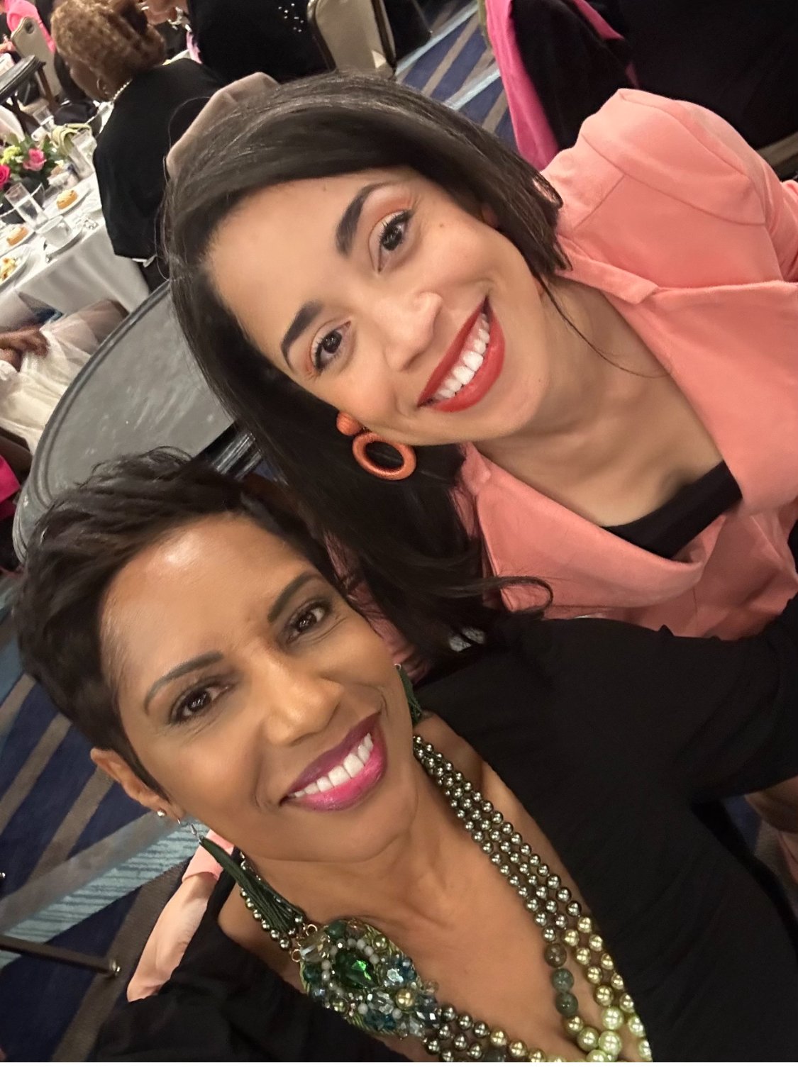Two women smiling at a formal event, wearing colorful clothing and accessories.