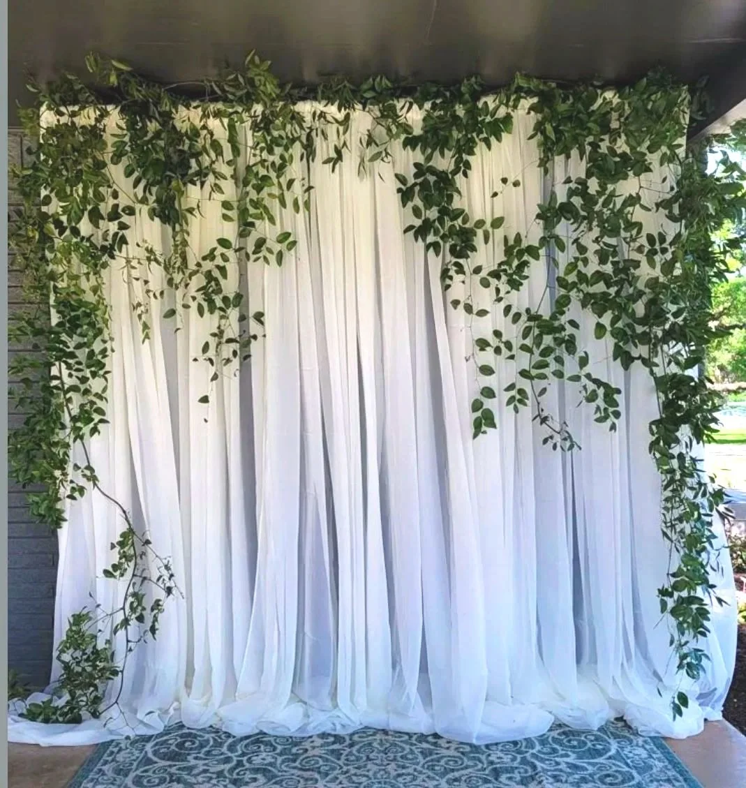 White curtain backdrop decorated with green leafy vines, with part of a patterned rug visible at the bottom.
